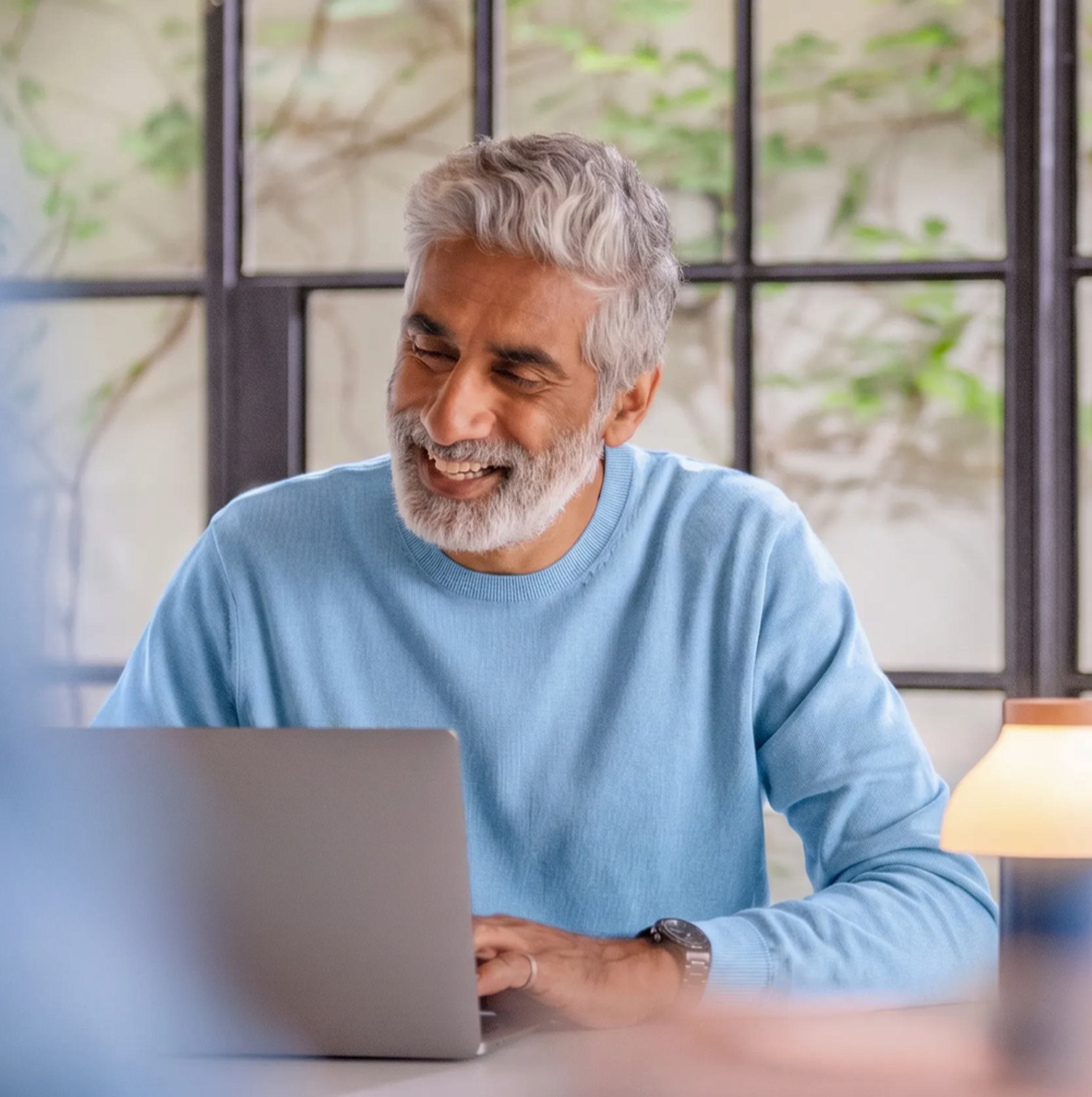 Proprietário sorrindo enquanto usa o notebook para gerenciar seu imóvel